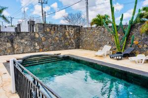 a swimming pool with chairs and a stone wall at Bliss Retreat Apartment Near Super U in Grand Baie
