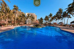 a large blue swimming pool with palm trees and buildings at Mexican Styled 2 BR Condo - Beachfront - Pool in Nuevo Nayarit