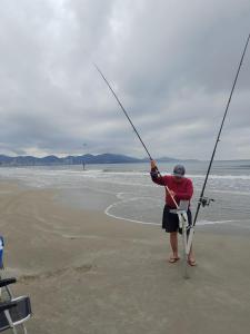 a person standing on the beach fishing on the beach at Lindo Apartamento compartilhado vista MAR in Itapema