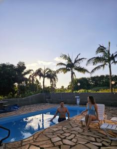 a man and a woman sitting next to a swimming pool at Refúgio GRUPOS com piscina, churrasqueiras 38 min Águas Claras Brasília in Brasilia