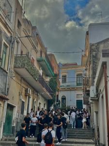 una folla di persone che camminano per una strada tra edifici di Scalinata del Nespolo Acitrezza ad Acitrezza