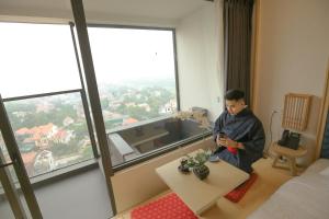 a man sitting in a hotel room looking at his cell phone at Căn hộ khách sạn wyndham Thanh Thuỷ in La Phu