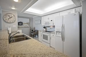 a kitchen with white appliances and a clock on the wall at New listing! Direct oceanfront condo with a balcony, heated pool, and tennis court in Bottle Island +41 photos