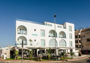 a white building with tables and umbrellas in front of it at Outsite Ibiza in Es Cana