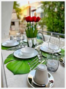 una mesa con platos blancos y flores rojas. en villa MeDITeRAN, en Pefkohori