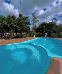 a large blue swimming pool with trees in the background at Chalés Pouso da Coruja - Vista para piscina in Cavalcante