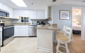 a kitchen with white cabinets and a bar with two chairs at Phoenix East 203 condo in Orange Beach