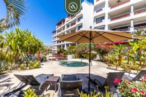 ein Sonnenschirm und Stühle und ein Pool vor einem Gebäude in der Unterkunft New 2 BR Condo in San Jose - Pool - Tennis in San José del Cabo