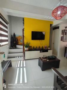 een woonkamer met een tv aan een gele muur bij Serene Home Stay in Puerto Princesa City