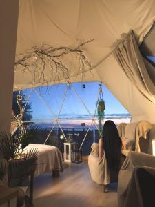 a woman sitting in a chair in a tent at Waterfront Glamping - Private hot tube, sauna & sunset view in Wapnica