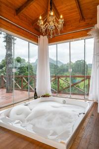 eine große weiße Badewanne in einem Zimmer mit einem großen Fenster in der Unterkunft Altos das Araucárias - one place, great moments! in Alfredo Wagner