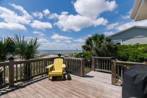 Una silla amarilla sentada en una terraza de madera con la playa. en Beach Retreat, en Edisto