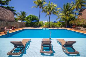 two lounge chairs and a swimming pool with palm trees at Pousada Barra Velha in Maragogi