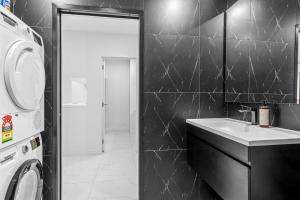 a black tiled bathroom with a sink and a washing machine at QV Stays Viaduct Harbour Elegance in Auckland +22 photos