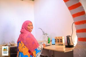 a woman standing in a kitchen with a table at Heissa Nubian Hostel in Aswân Reservoir Colony