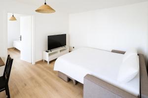 ein weißes Schlafzimmer mit einem Bett und einem Fernseher in der Unterkunft Séjour cosy près de Strasbourg avec parking in Souffelweyersheim