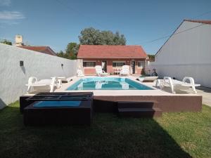 a swimming pool with white chairs and a house at Casa con pileta,quincho ymas servicios para vos in Santa Teresita