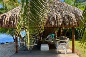 a hut with chairs and a table on the beach at Villa Ohana - 4BR Beachfront Villa in Paopao