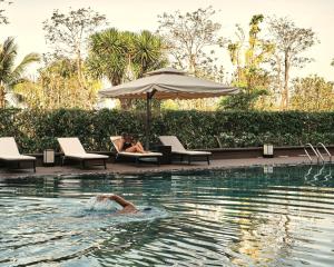 una persona che nuota in una piscina con un ombrellone di Kobi Onsen Resort Hue, Affiliated by Melia a Hue