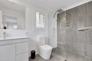 a white bathroom with a toilet and a sink at Beautiful Family House with Pool and BBQ in Gold Coast +24 photos