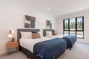 two beds in a room with white walls and windows at The Riverside House in Burradoo