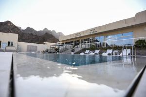 a swimming pool with chairs and a building at paradise resort and spa in Hatta