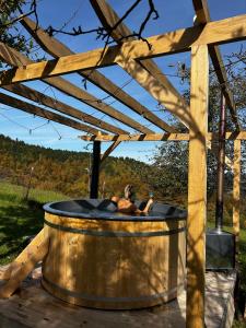 un uomo in una vasca idromassaggio sotto un pergolato di legno di GLAMPING BRUNDO - Tents and Cottage with SAUNA & JACUZZI a Kostel