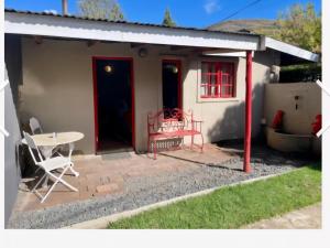 una pequeña casa con una puerta roja y una mesa en Bella Rosa Cottage, en Clarens
