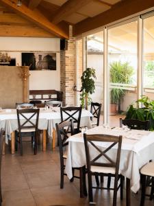 Un restaurante con mesas y sillas blancas y ventanas. en Il Castagno, en Orciano di Pesaro