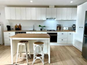 una cocina con armarios blancos, mesa y taburetes en Cosy Guesthouse in Moss Vale, en Moss Vale