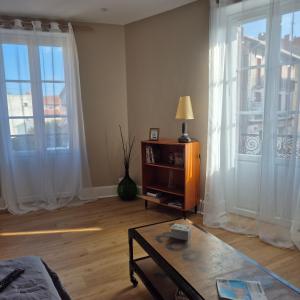 a living room with two large windows and a table at Chez Armande 2 étoiles in Châtel-Guyon