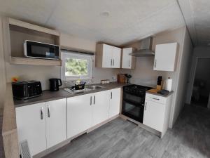 a kitchen with white cabinets and a sink and a microwave at Cow & Calf Cottages- bike wineries & relax in rural location Napier 15 mins in Puketapu