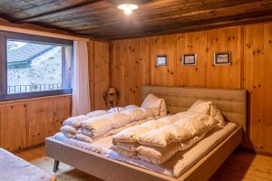 a bed in a room with wooden walls and a window at Sunny, rustical 5 room cottage in Valposchiavo in Poschiavo