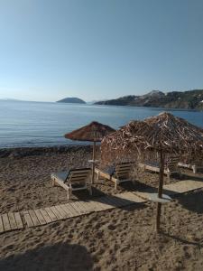 two chairs and umbrellas on a beach with the ocean at Vromolithos apartments in Nisís Léros
