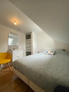 a white bedroom with a bed and a yellow chair at Duplex quartier calme et parking gratuit in Amiens