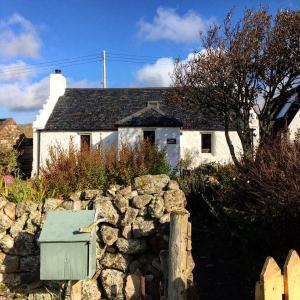 una pared de piedra frente a una casa blanca en Raven Cottage, en Rhiconich