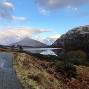 a road next to a lake with mountains in the background at Raven Cottage in Rhiconich
