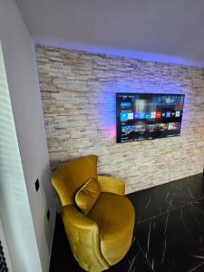 a yellow chair in front of a brick wall with a tv at Cristina Apartment in Râşnov