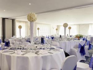 a room filled with tables with white tablecloths and chairs at Mercure Thame Lambert Hotel in Chinnor