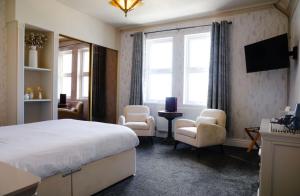 a bedroom with a bed and chairs and a television at The Lilly Restaurant With Rooms in Llandudno