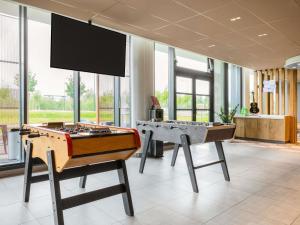 two ping pong tables in a room with windows at ibis Gonesse Le Bourget in Gonesse