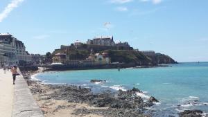 Una mujer caminando por una playa con un castillo en una colina. en Cryste Marine, en Granville