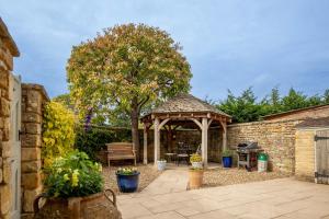 a wooden gazebo with a bench and a tree at Old Orchard Cottage in Moreton in Marsh