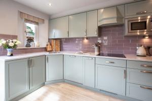 a kitchen with white cabinets and purple tiles at Old Orchard Cottage in Moreton in Marsh