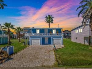 a large blue house with palm trees in front of it at Cozy beach bungalow close to ocean with large yard in Galveston