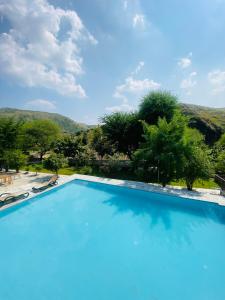 une grande piscine bleue avec des montagnes en arrière-plan dans l'établissement The Mudcasa, à Udaipur