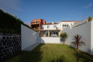 a backyard with a white wall and a grass yard at Figueiras House Pópulo Beach in Ponta Delgada