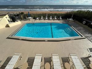 a swimming pool with chairs and the ocean in the background at Renovated direct oceanfront condo with spacious balcony, heated pool, and garage parking in Ormond-by-the-Sea