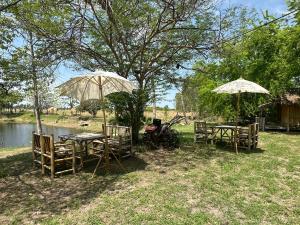 a group of tables and umbrellas next to a river at มีสุข ฟาร์มสเตย์ in Lop Buri
