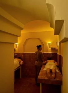 a woman standing in a bathroom with a person laying on a table at Hotel Al Alba Hammam & Restaurant in Asilah